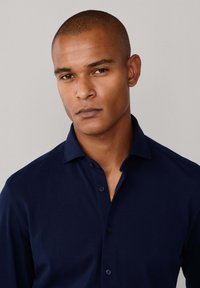 Marineblauwe button-up overhemd met een kraag, textuurstof en een slanke pasvorm. Vier knopen zichtbaar aan de voorkant, met een subtiele glans.