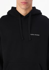 Čierna mikina s kapucňou vyrobená z mäkkého materiálu, s prednou kapsou, sťahovacou kapucňou a malým bielym logom "STYLE & SCOTT" na hrudi.