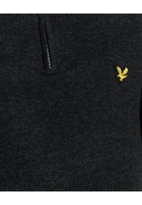 Mörkgrå zip-up tröja i stickad textur, med en liten gul örnlogotyp på vänster sida. Dragkedjan går halvvägs ner på framsidan.