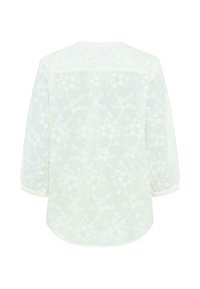 Blouse blanche à manches longues avec motif en dentelle florale, ourlet arrondi et manches avec poignets, vue de dos sur un fond uni.