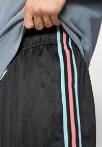 Mustad lühikesed püksid on roosa ja helerohelise vertikaalse triibuga. Kangal on tekstuuriga välimus ning osaliselt on nähtav elastne vöökoht.