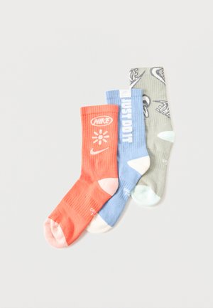Drie Nike crew-sokken in koraal, lichtblauw en grijs met logo's en de tekst "JUST DO IT" op het lichtblauwe paar, met witte teen- en hielaccenten.