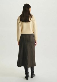 Pull en laine beige à manches longues associé à une jupe rayée verte foncé arrivant au milieu du mollet, portée avec des bottes noires hautes jusqu'aux genoux.