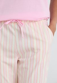Calças de pijama às riscas em amarelo claro com finas linhas em rosa e laranja, apresentando uma cintura elástica com cordão e bolsos laterais.