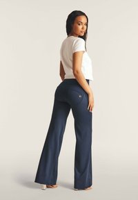 Laudan leveälahkeiset housut, joissa on sileä kangaspinta, kahdella takataskulla ja metallisilla yksityiskohdilla. Yhdistetty napakasti istuvan valkoisen t-paidan kanssa.