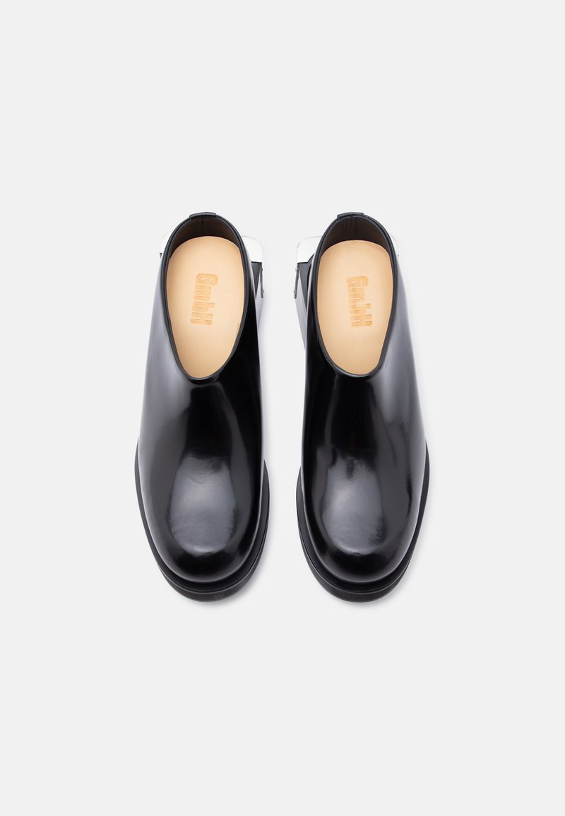 Pair of black glossy slip-on shoes with beige insoles, viewed from above on a white background.