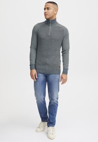 Gray, textured half-zip sweater with raglan sleeves, paired with blue jeans and white sneakers. Notable leather accent at the hem.
