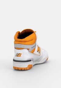 Wysokie sneakersy z białej skóry z pomarańczowymi akcentami. Charakteryzują się wyściełanym kołnierzem, regulowanym paskiem oraz teksturowaną gumową podeszwą dla lepszej przyczepności.