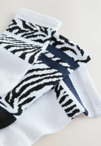 Tri par čarapa s uzorkom zebra pruga u crno-bijeloj boji s plavim akcentima, rebrastom teksturom i kombinacijom jednoličnih i uzorčanih dijelova.