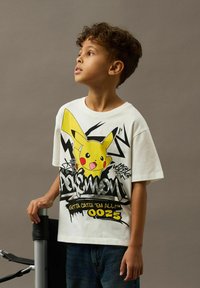 White short-sleeve t-shirt featuring a Pikachu graphic, bold black and yellow accents, and text that reads "Pokémon" and "Gotta Catch 'Em All! 0025."