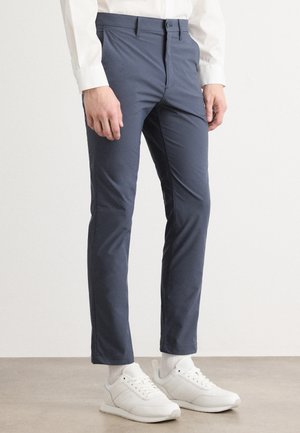 Marineblaues Slim-Fit-Hosendesign aus glattem Material mit klassischem Bund und vorderen Taschen, kombiniert mit weißen Sportschuhen.
