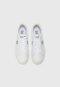 Tenisi sintetici albi cu vârfuri rotunde, șireturi plate și branding pe lateral. Textură netedă și design minimal.