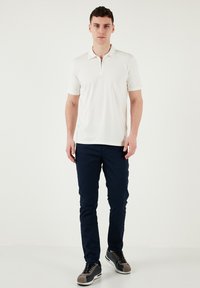 Weißes kurzärmeliges Poloshirt mit Reißverschlusskragen, kombiniert mit marineblauen Slim-Fit-Hosen und grauen Sneakers. Glatte Textur, schlichtes Design.