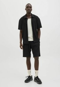 Black ribbed short-sleeve shirt, white ribbed tank top, black shorts, black sneakers, and light-colored socks with logo detail. Simple design.