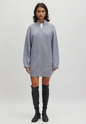 Hellgraues Strickkleid mit einem Viertelreißverschluss-Kragen, Fallerschultern, gerippter Textur und langen Ärmeln, kombiniert mit schwarzen kniehohen Stiefeln.