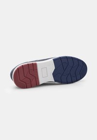 Sole of a shoe featuring a patterned tread, with a navy, white, and red color scheme and a significant rubber texture for traction.