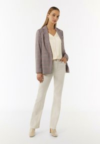 Blazer mit einem mehrfarbigen Karomuster, cremigem Oberteil und hellbeigen Schlaghosen. Glatte Textur und minimalistisches Design. Neutralfarbene Absätze.