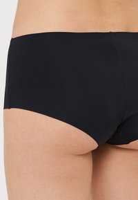 Svart bikinitruse med glatt, elastisk stoff, lavt liv og enkelt design. Sømløse kanter for komfort og minimal detalj.