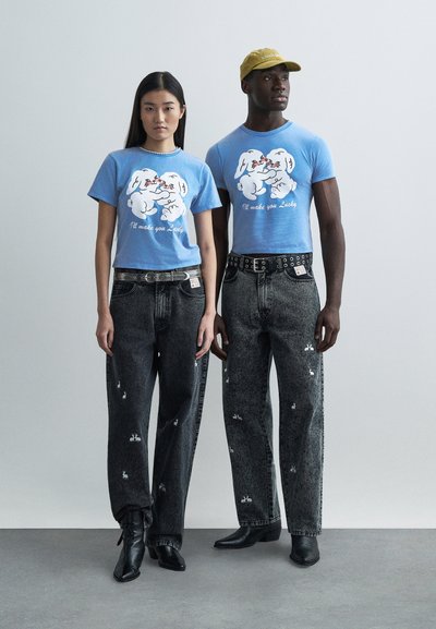 Blå grafiska t-shirts med tecknade kaniner och texten "Jag gör dig lycklig." Komplett med svarta denimbyxor med kaninmönster.