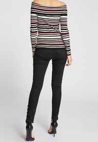 Bluzka w paski odkrywająca ramiona w kolorach czarnym, białym i czerwonym o prążkowanej fakturze; zestawiona z czarnymi obcisłymi dżinsami i szpilkami.