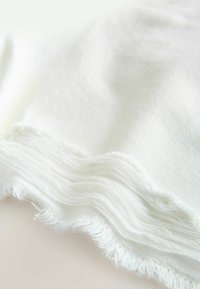 Tissu blanc doux avec une texture tissée fine, présentant des bords légèrement effilochés et des couches délicates pliées ensemble.