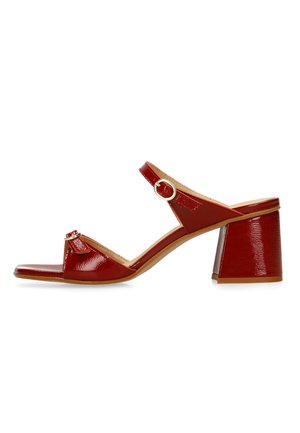 Rode lakleren open-toe sandaal met blokhak en enkelbandje met gouden gesp op witte achtergrond.