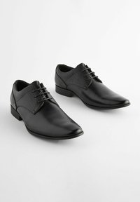 Zapatos de vestir de cuero negro con puntera afilada, que cuentan con un panel superior texturizado y seis ojales para los cordones. Suela resistente y acentos de diseño mínimos.