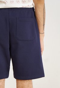 Shorts en coton bleu marine avec une poche arrière, présentant une texture lisse et une coupe droite, idéaux pour un usage décontracté.