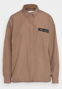 Hnědá košile s dlouhým rukávem a knoflíky, na levé kapse černá nášivka s nápisem "esmé studios", límeček a skryté knoflíky.