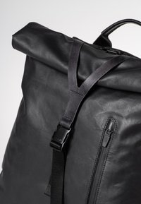 Zaino nero a forma di roll-top realizzato in pelle resistente, dotato di chiusura con fibbia, superficie texturizzata e una tasca laterale con zip per un facile accesso.