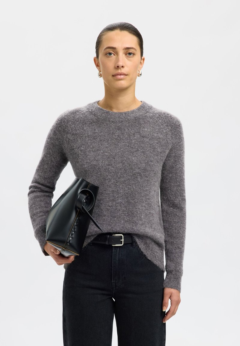 Sivi volnen pulover s klasičnim okroglim izrezom in rebrastimi manšetami, kombiniran s črnimi kavbojkami z visokim pasom ter strukturirano črno torbico.