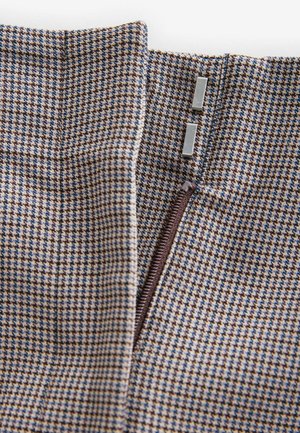 Braun und blau gemusteter Stoff mit einem dezenten Hahnentrittmuster. Verfügt über einen Reißverschluss mit braunem Zipper und zwei rechteckigen Metallakzenten.