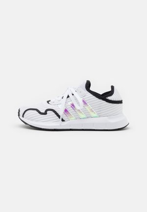 Chaussure de sport blanche avec bordure noire, trois bandes irisées sur le côté, lacets blancs et semelle noire et blanche, vue du côté intérieur.