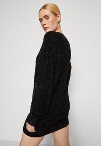 Vestito a maglia nero glitterato, maniche lunghe, vestibilità comoda, texture morbida e leggero lucido, che si ferma poco sopra la coscia.