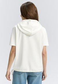 Witte hoodie met korte mouwen en een relaxte pasvorm, met een trekkoord aan de onderkant en een textuurstof. Eenvoudig ontwerp zonder versieringen.