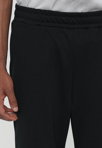 Sorte sportbukser med elastisk talje, lavet af glat, let materiale. Har en sidelomme og en tapered ben design.