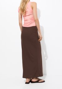 Haut ajusté rose avec détails froncés, associé à une jupe longue marron jusqu'au sol, porté avec des tongs plates. Design simple, texture lisse.