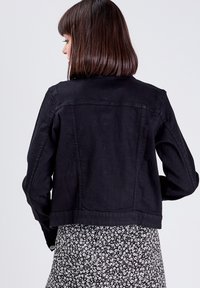 Chaqueta de mezclilla negra con un corte cropped, que presenta un diseño sencillo, detalles de costura sutiles y mangas largas.