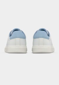 Λευκά αθλητικά παπούτσια με τακούνι από γαλάζιο σουέτ, επάνω μέρος από λείο δέρμα και υφασμένο ελαστικό πάτο, που παρουσιάζουν μινιμαλιστικό σχεδιασμό και καθαρές γραμμές.