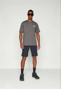 Gray short-sleeve t-shirt with a small logo, paired with navy shorts and black hiking shoes. Sunglasses complete the look.