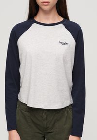 Szara i granatowa longsleeve z krótkim krojem i okrągłym dekoltem. Haftowane logo "SuperDry" na klatce piersiowej. Miękki materiał.