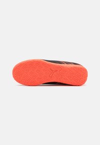 Suela de zapatilla de correr negra con un patrón texturizado naranja, que presenta surcos para tracción y un logo en el centro.