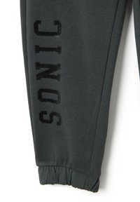 Grijze joggingbroeken van zachte stof hebben een geribde manchet en het woord "SONIC" in het zwart gedrukt op het linkerbeen.