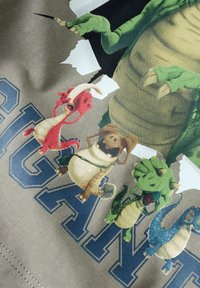 Groene stof met een cartoon-draken en drie kleinere wezens, met de vette tekst "SUGAN" eronder. Het ontwerp bevat kleurrijke accenten en texturen.