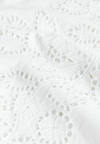 White fabric with intricate floral embroidery and cut-out lace patterns, showing texture and delicate stitching details.
