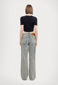 Czarna krótka koszulka w połączeniu z jasnoniebieskimi szerokimi spodniami dżinsowymi. Spodnie mają brązową skórzaną metkę z logo na tylnym pasku.