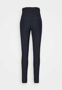 Pantalon noir à fines rayures, fuselé, avec taille élastique paperbag et deux poches passepoilées à l'arrière, vu de dos.