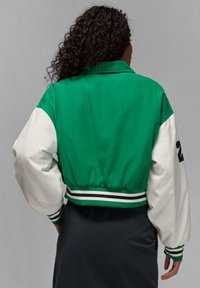 Zaļš un balts bomber jackets ar elastīgu jostu, svītrainiem akcentiem un apjomīgām piedurknēm. Gluda auduma ar sportisku dizainu.