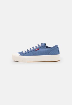 Baskets basses en toile bleue avec semelle et embout en caoutchouc blanc, lacets blancs et petite étiquette rouge avec le logo Levi's sur le côté.