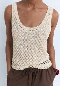 Knit sleeveless top with an open mesh design, in light beige. Features a wide scoop neckline and a scalloped hem.
